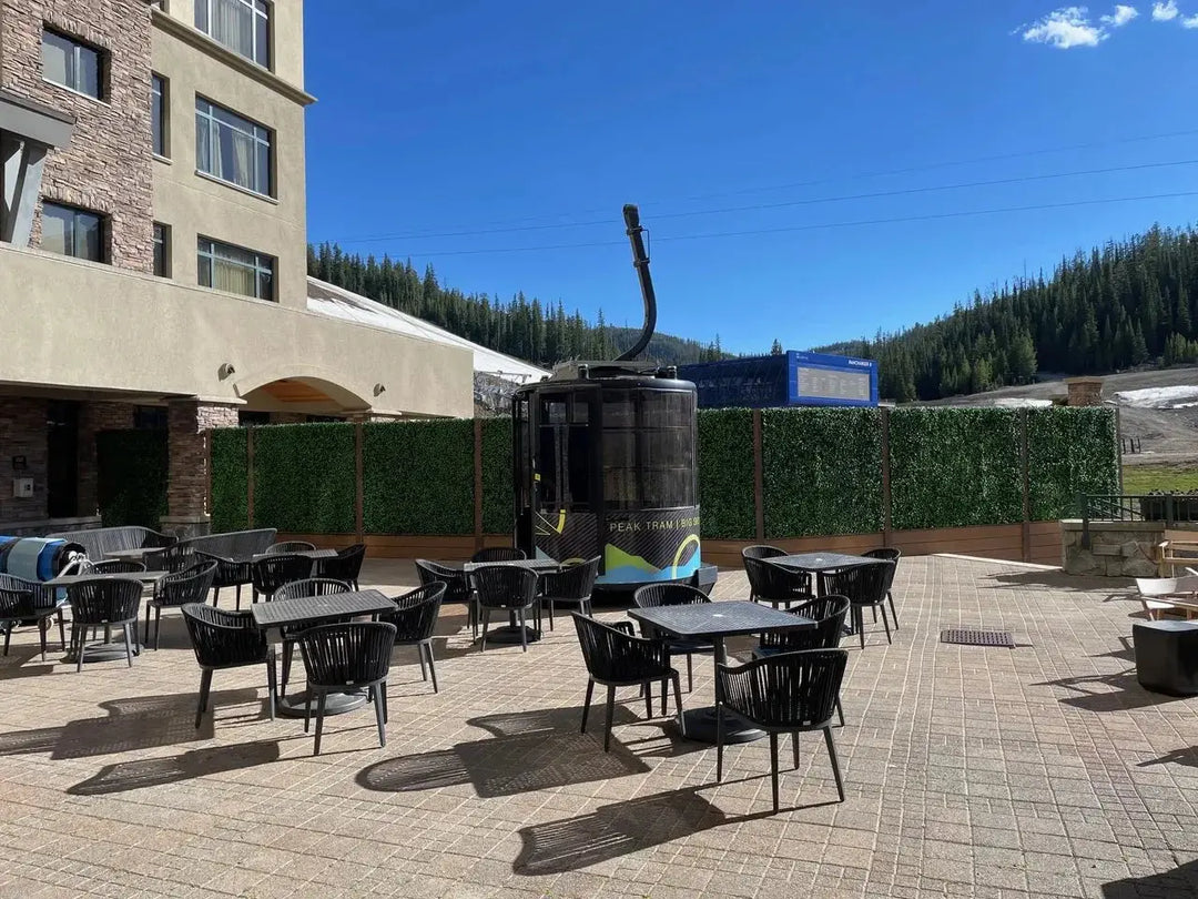 Outdoor seating area with black chairs and artificial green plant wall panels.