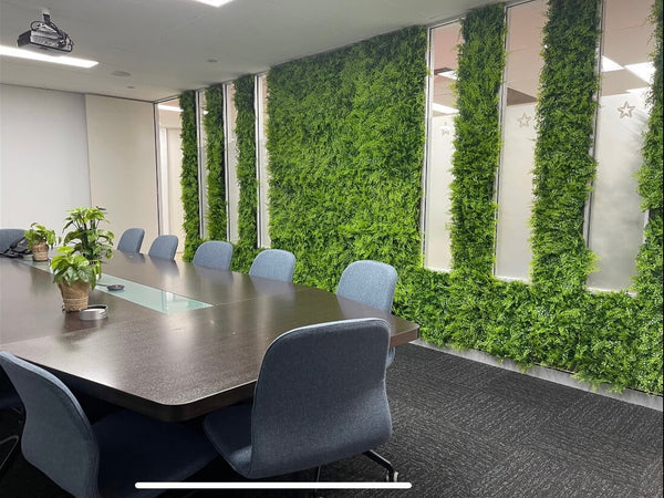 Boardroom table and chairs beside vertical strips of artificial green wall