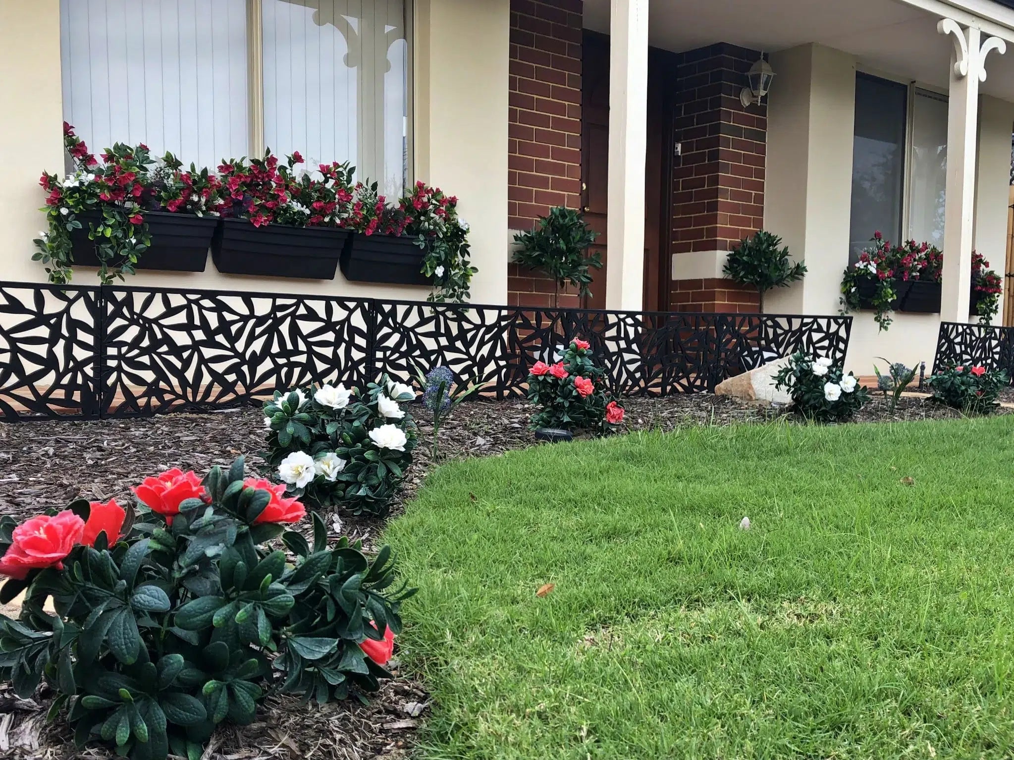 A house with a (5 Pieces) Vibrant Pink Hanging Artificial Bougainvillea Plant, UV Resistant 35" in a flower bed in front of it.