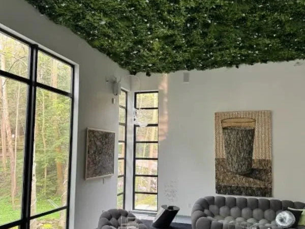 Artificial greenery covering the ceiling above a lounge with grey sofas