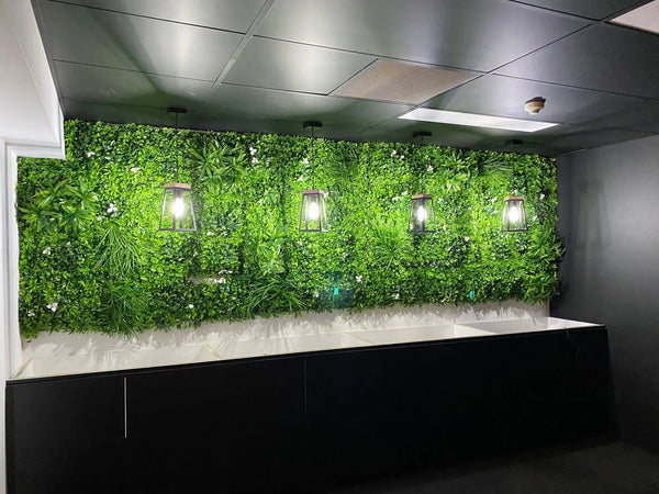 Artificial green wall with white flowers and pendant lights above a dark counter