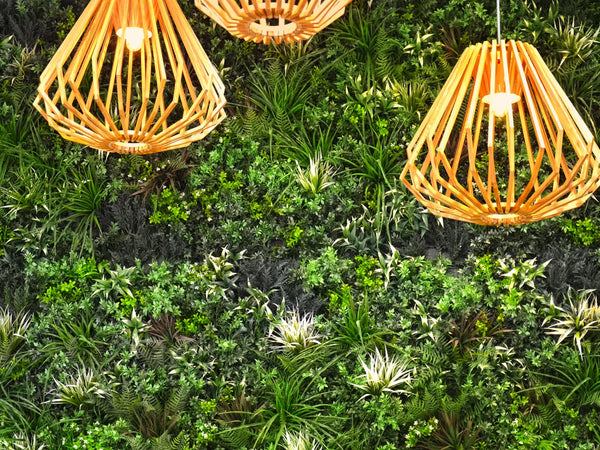 Three woven pendant lights hanging in front of an artificial green wall in a shopping center