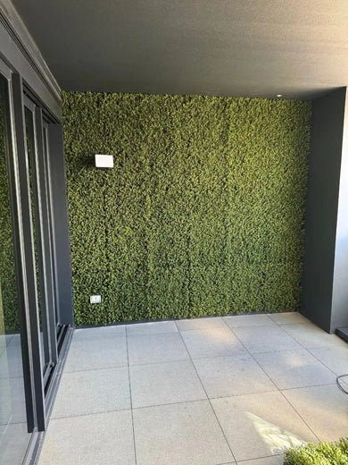 Green artificial grass wall in a modern indoor setting with gray flooring.