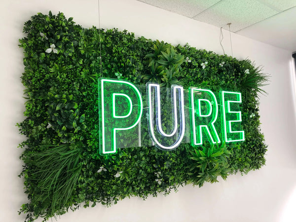 Illuminated neon sign mounted on an artificial green wall panel in a shop