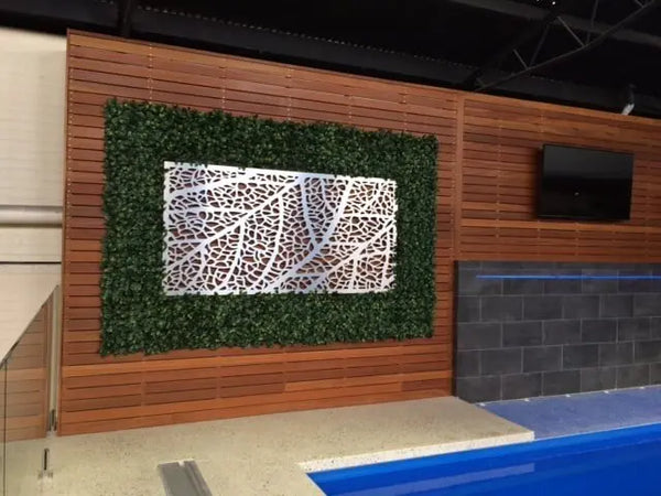 Artificial hedge panel with metal leaf wall art on a timber-clad shop display wall
