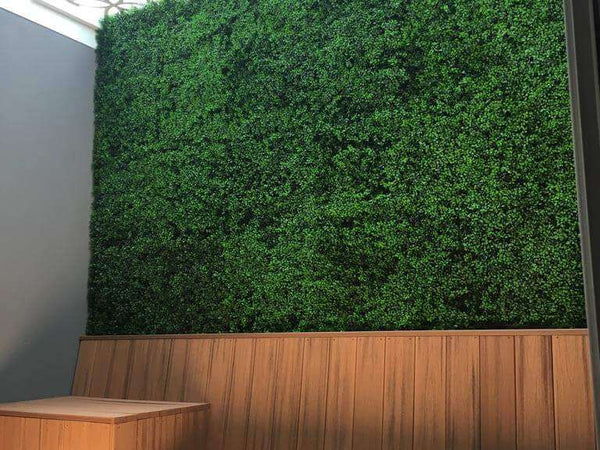 Faux boxwood hedge panel above timber bench seating in a cafe outdoor area