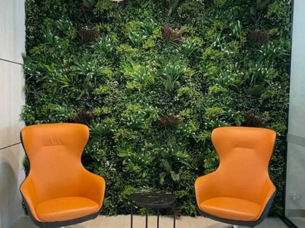Two orange lounge chairs and pendant lights in front of a leafy green wall in a waiting area