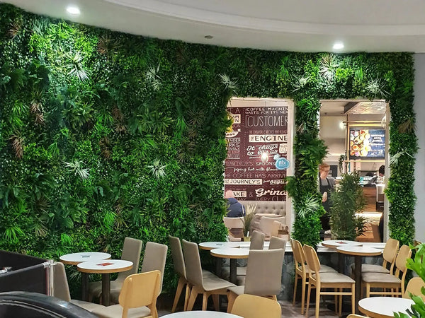 Cafe tables and chairs in front of a large artificial green wall around a serving window