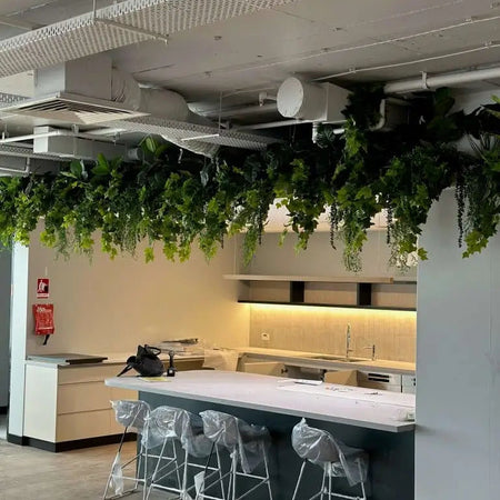 Artificial hanging plants suspended above an office breakout bench with stools.