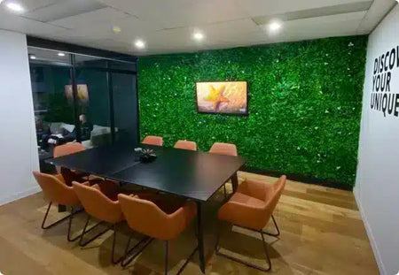 Conference room with an artificial green wall behind a long table and orange chairs.