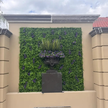 Artificial vertical garden behind a stone fountain in a Mediterranean-style courtyard.