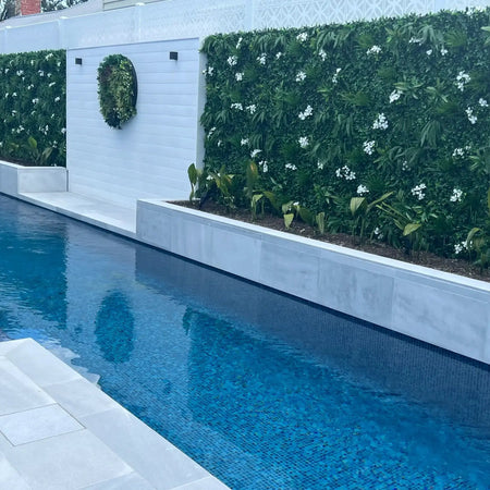 Artificial green wall panels along a white wall beside a lap pool.