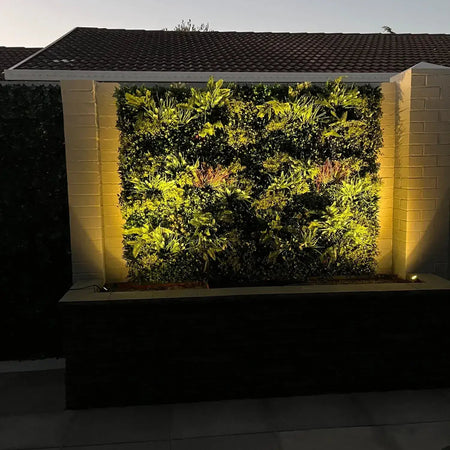 Artificial green wall lit by warm uplights at night in an outdoor venue.