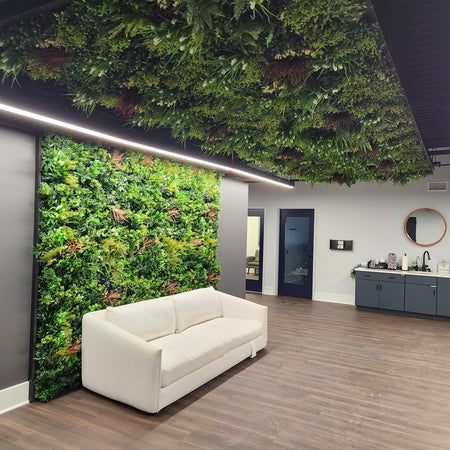 Office reception with an artificial green wall behind a white sofa and artificial greenery across the ceiling.