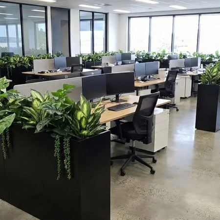 Long planter boxes filled with artificial greenery dividing desks in an open-plan office.