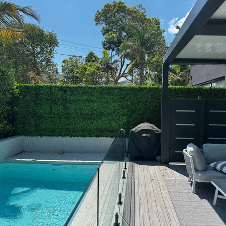 Artificial hedge panels behind a glass pool fence and wood deck.