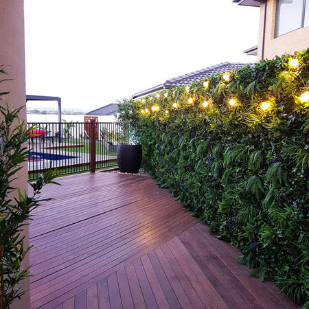 Rooftop deck with string lights and an artificial green wall along the railing.