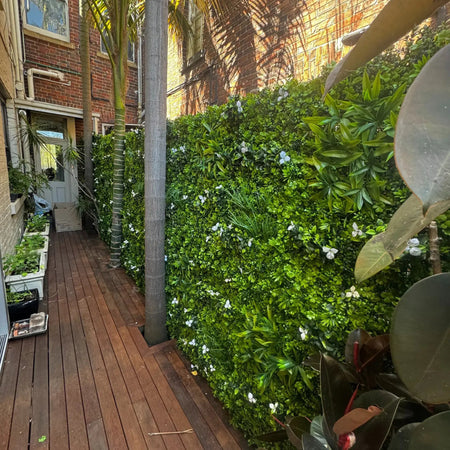 Artificial hedge panels lining a wooden side passage beside a house.
