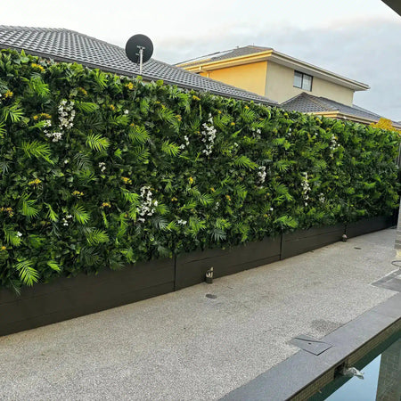 Tropical-style artificial green wall along a boundary fence above a planter.