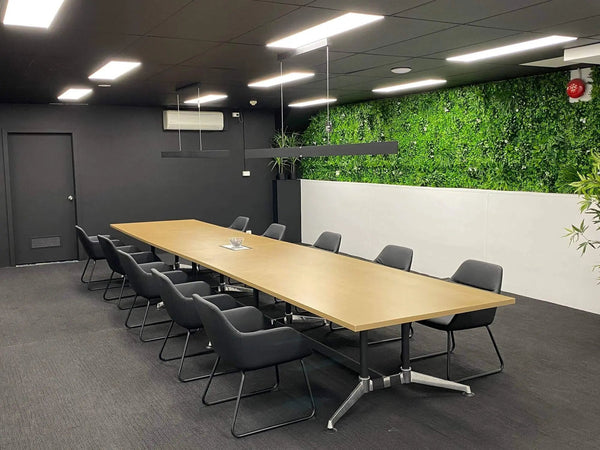 Long meeting table and chairs beside a full-length artificial green wall in an office meeting room