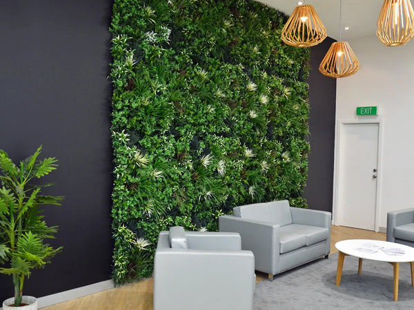 Grey lounge chairs and a round table in front of an artificial green wall with pendant lights in a shopping center