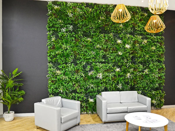 Shopping center seating area with grey sofas and a coffee table in front of a large artificial green wall